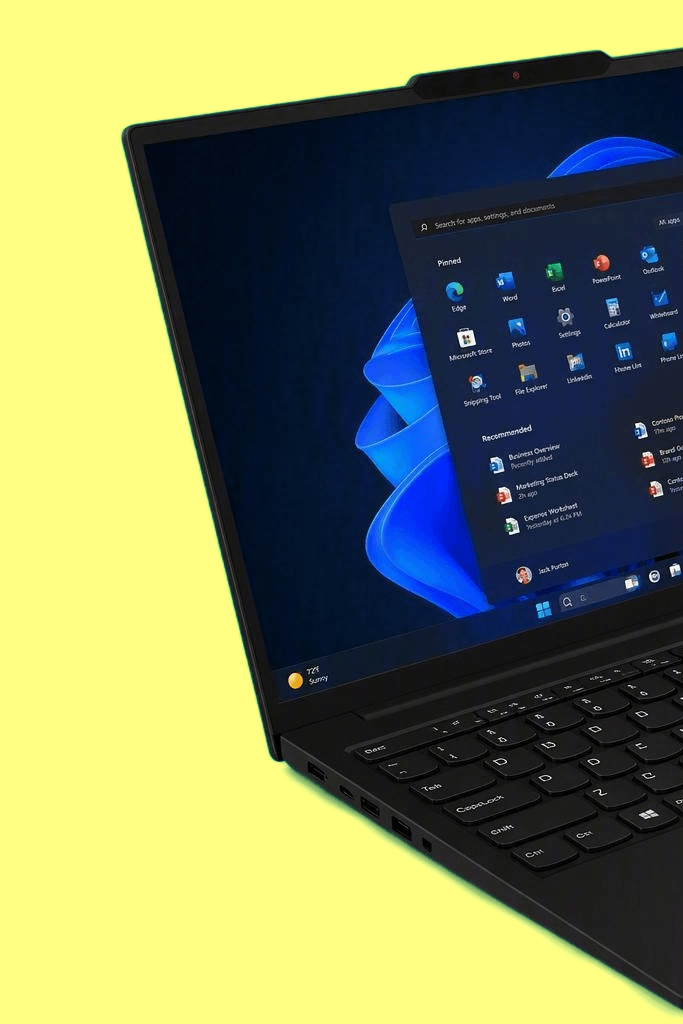 A black Lenovo ThinkPad laptop shown open at an angle against a bright yellow background. The screen is on and displays a blue-themed Windows desktop with an app window open.